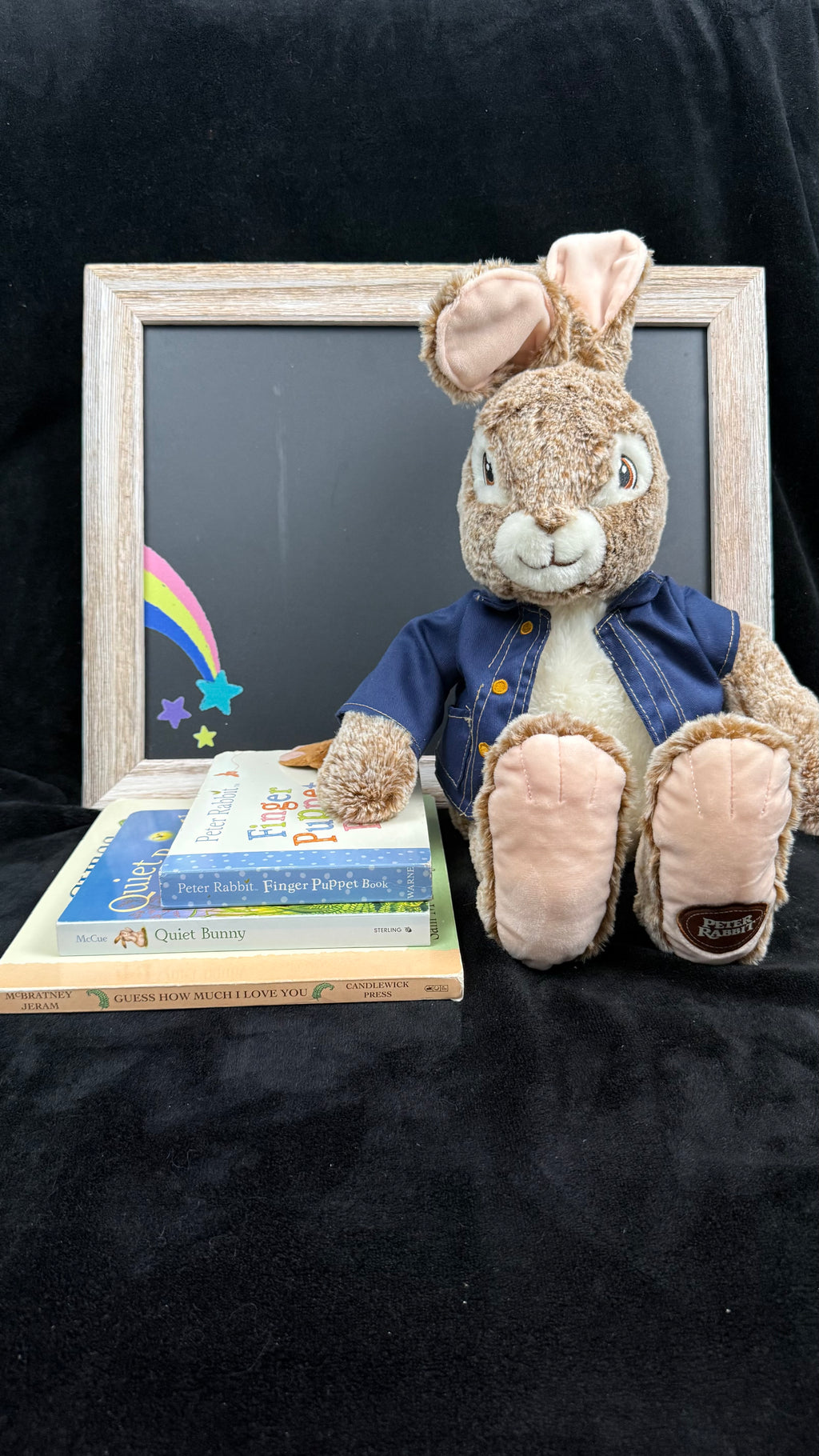 Peter Rabbit plush resting a paw on the stack of three bunny board books